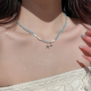 Détail de pendentifs étoile et coquillage sur un collier de perles bleues sur un modèle