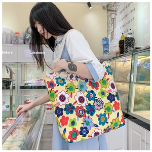 Detailed view of yellow floral canvas tote bag with tassel worn by a model in a shop