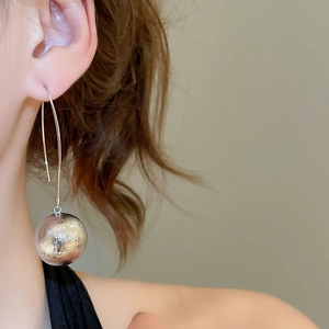Detailed close-up of a silver textured sphere pendant on a stylish metal hook earring