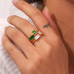 Close-up of gold rings set with green and white rectangular gemstones on a model's hand