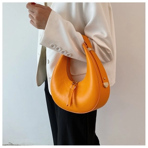 Detail of vibrant orange crescent shoulder bag held by a model in a white blazer