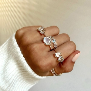 Close-up of hand wearing multiple gold rings with pear and emerald cut moonstone zircons