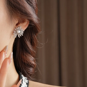 Detailed close-up of a silver sunflower pearl earring with crystals on model ear