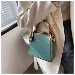Detail of turquoise box bag with gold metal frame, silk scarf handle, and chain strap
