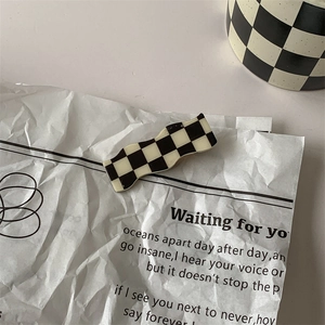 Detail of wavy black and white checkerboard acetate hair clip on vintage paper
