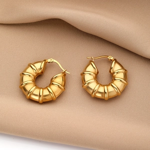 Detail of chunky gold geometric hoop earrings with radiant texture on silk background