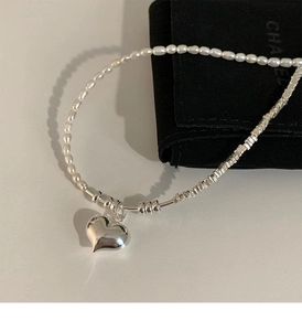 Detail of trendy necklace featuring white pearls and silver heart pendant on a velvet pouch