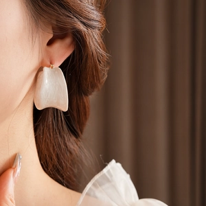 Close-up of white marble pattern resin hoop earrings on model in soft warm lighting