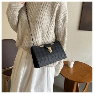 Detail of black woven shoulder bag with golden twist lock and chain strap on a model