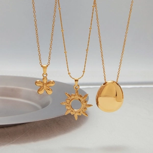 Detailed view of three 18k gold-plated necklaces with flower and sun pendants on white plates