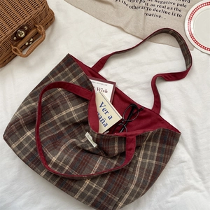 Flat lay of large plaid tote bag with books and glasses on white wrinkled fabric