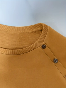 Detail of ginger knit sweater featuring ribbed crew neck and two dark shoulder buttons