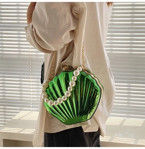Detail of green shell clutch bag with pearl handle and golden chain on model
