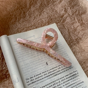Detailed view of pink marble acetate shark clip with gold alloy teeth on vintage book