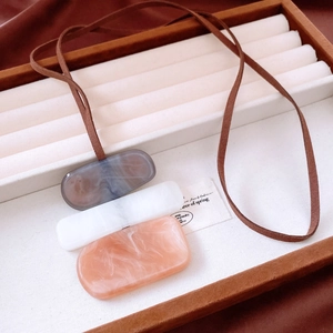Macro detail of acrylic marble charms on a long necklace in a beige jewelry box