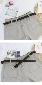 Détail d'une fine ceinture en cuir noir avec boucle dorée sur un short en jean