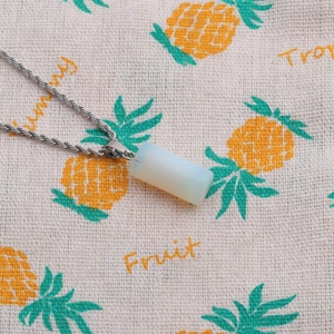 Detail of a milky white stone cylinder pendant with a silver twisted chain on fabric