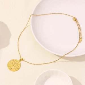Detailed close-up of a gold stainless steel tree of life pendant on a white porcelain dish