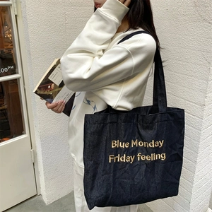 Detail of gold letter embroidery on dark blue denim tote bag with textured fabric