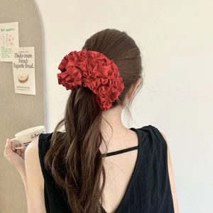 Detail of a large burgundy satin scrunchie with pleated edges on a woman's hair
