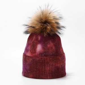 Detailed close-up of colorful tie-dye knit beanie with large fluffy faux fur pompom