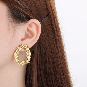 Macro detail of gold leaf pattern circular earrings worn by a model in soft lighting