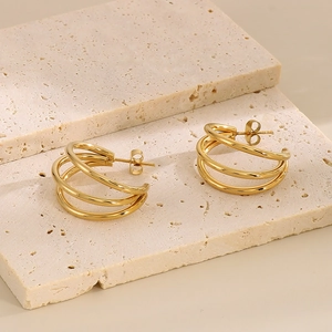 Macro detail of gold triple-layered C-shaped stud earrings on a textured stone base