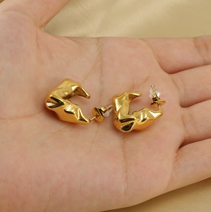 Detail view of gold wave textured geometric hoop earrings held in a person's hand