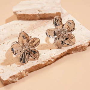 Close-up of silver flower earrings with wavy petals on a textured stone display