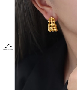 Close-up of gold stainless steel C-shaped beaded earrings worn on ear model