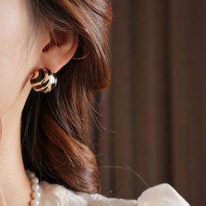 Detail of round gold and black enamel stud earring on model with elegant jewelry