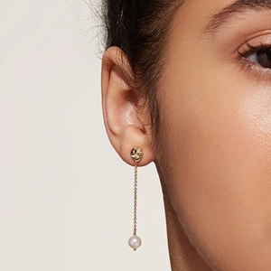Close-up of gold tassel chain earring with white round pearl on female model ear