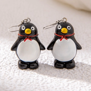 Cartoon penguin stud earrings with red bowties on white textured fabric background
