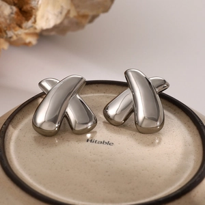 Detailed view of silver polished chunky X-shaped cross earrings on a ceramic display