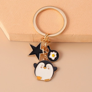 Cute penguin keychain with golden ring featuring a black star and a fried egg pan charm