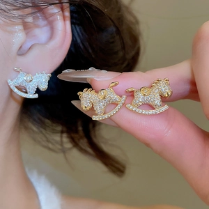 Detail of rocking horse stud earrings in gold and silver finish with crystal pavé