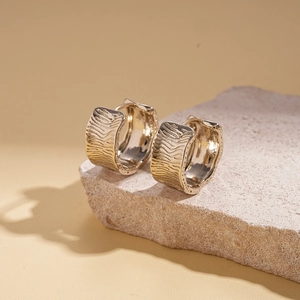 Detail of 18K gold-plated earrings with wavy textures on a stone pedestal