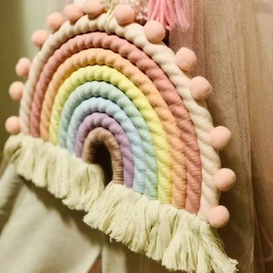 Detailed view of handmade woven rainbow wall hanging with pink pompoms and tassels