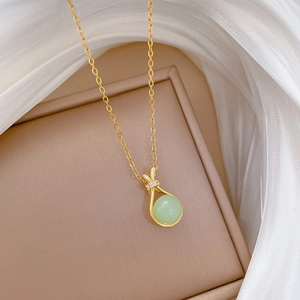 Macro shot of gold necklace with round light green gemstone pendant on soft fabric