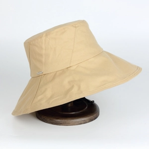 Detail view of khaki sun hat featuring a metal nameplate and adjustable windproof cord