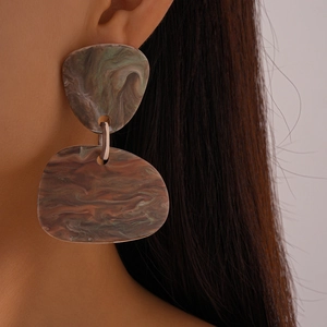 Close-up of model wearing resin geometric earrings with green and brown marble texture
