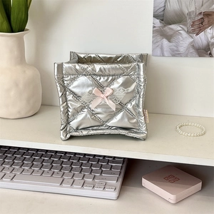 Detail of silver quilted storage box with white lace wings and pink ribbon bow on a desk