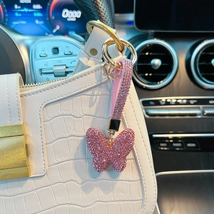 Close-up of pink crystal butterfly keychain with rhinestones hanging on a luxury white handbag