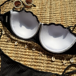 Detail of black scalloped bikini with seashell and starfish charms on ribbed fabric