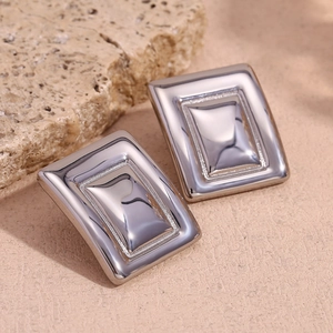 Macro shot of silver geometric rectangular earrings on a textured stone background
