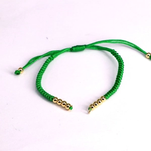 Detail view of emerald green woven cord bracelet with adjustable pull closure and gold beads