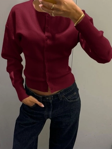 Détail d'un cardigan en tricot rouge foncé avec poignets côtelés et fermeture boutonnée