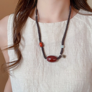 Detail of wax rope necklace with red agate stone and engraved metal charm on a model
