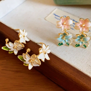 Close-up of floral stud earrings with enamel petals and gold plating on a wooden tray