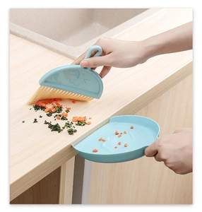 Close-up of blue mini handheld broom and dustpan set cleaning debris on wooden surface